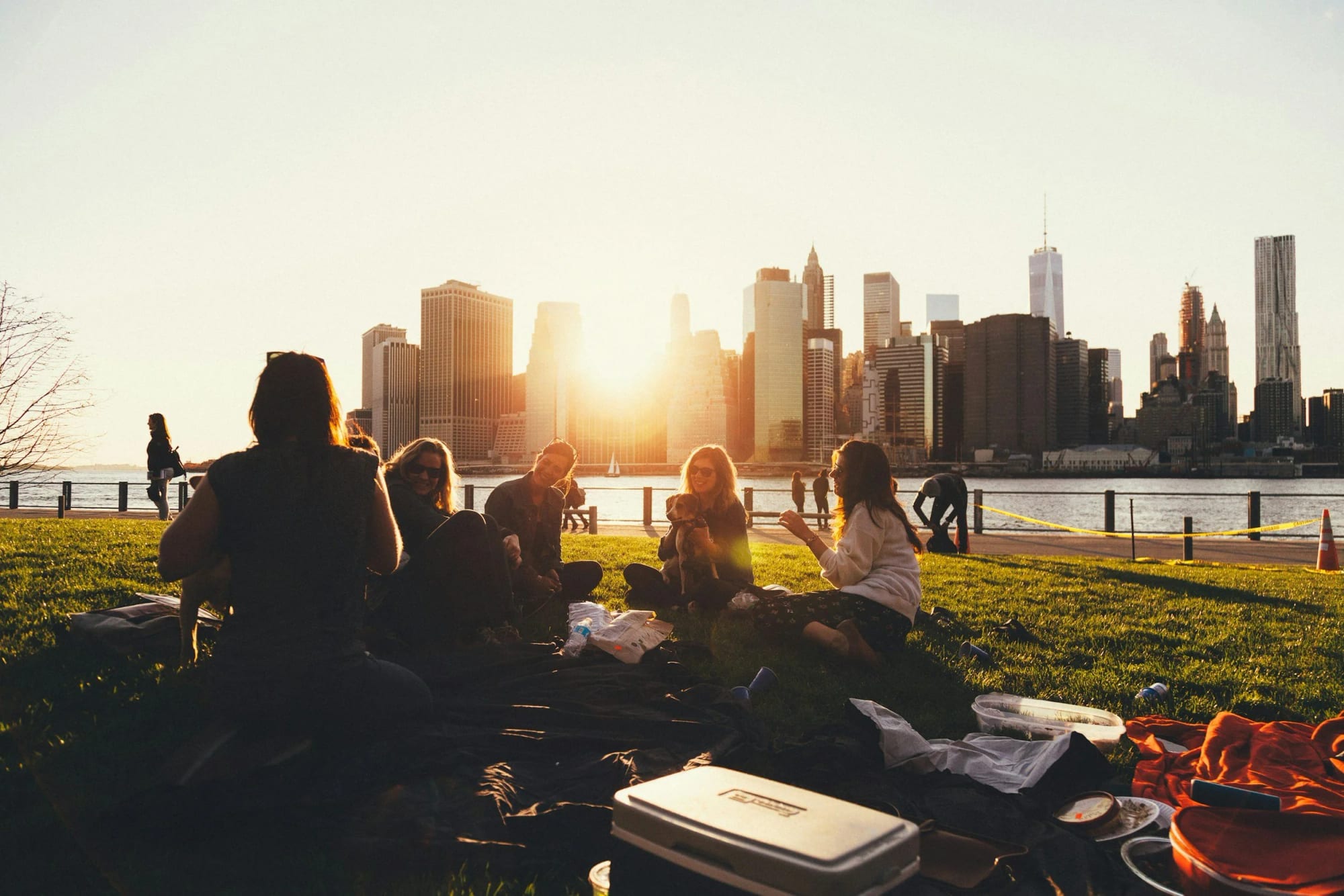 A group of young adults gathered for a picnic at sunset, with a city skyline behind them